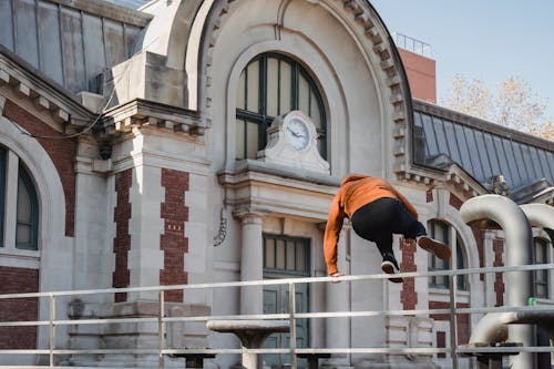 Sportive man jumping over railing near old historic building