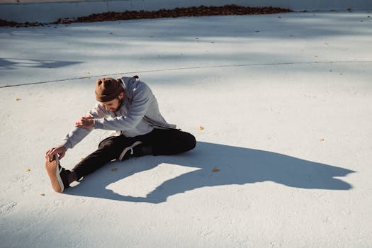 Attentive slender sportsman in casual clothes leaning forward while working out on urban pavement with shadow in sunlight