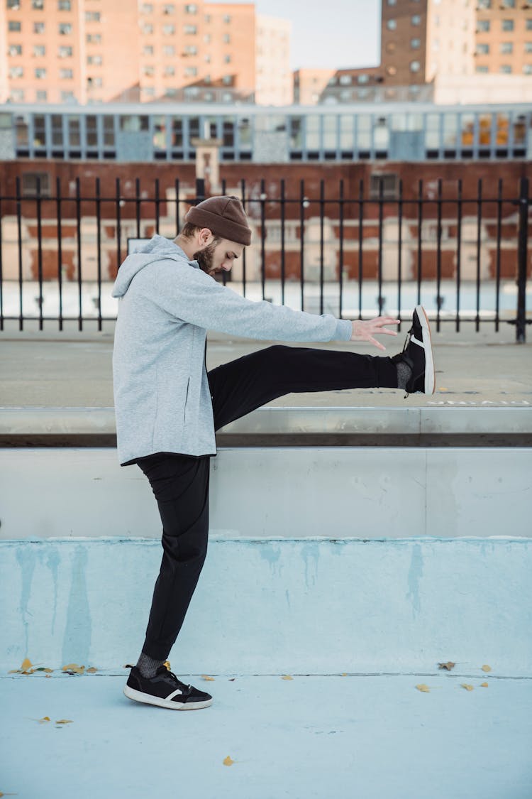 Man In Casual Clothes Standing With Raised Leg On City Street