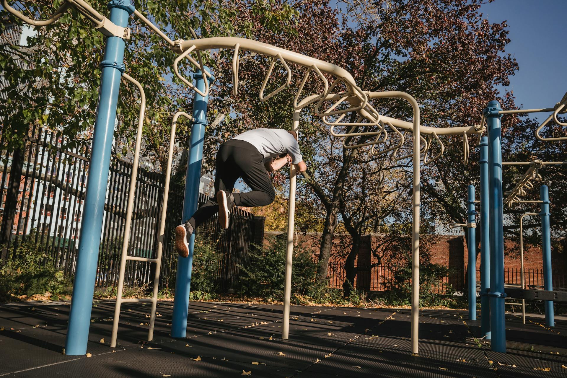 Faceless male exercising on pole near turnstile in park