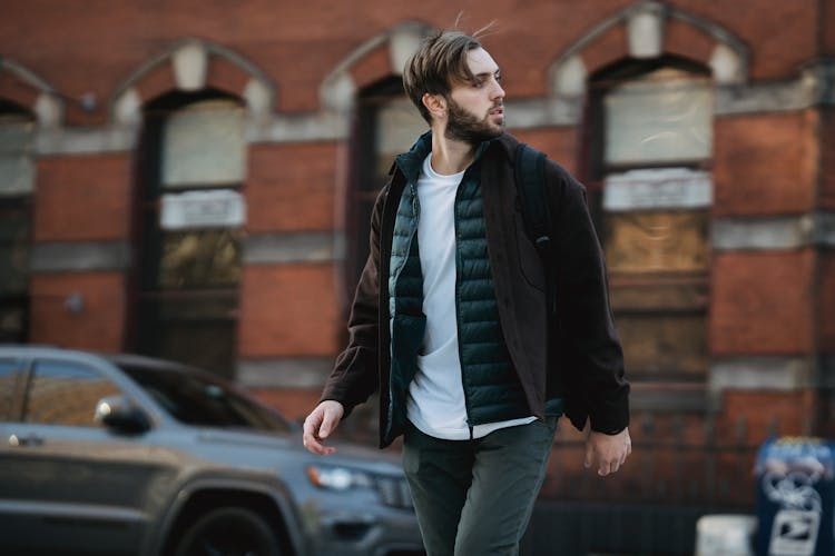 Guy Walking On Street Near Car And Building In Town