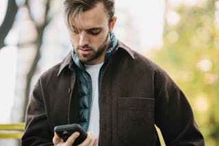 Young hipster looking at smartphone screen in park