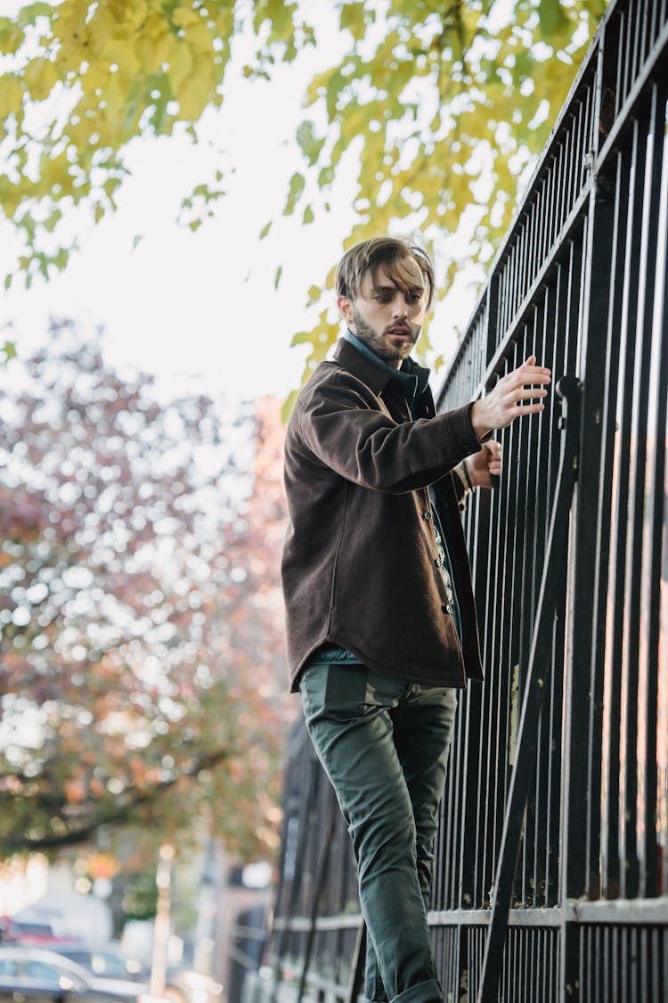 Stylish Young Man Holding To Metal Fence