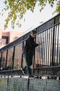 Side view of young handsome man in stylish outfit walking near metal fence