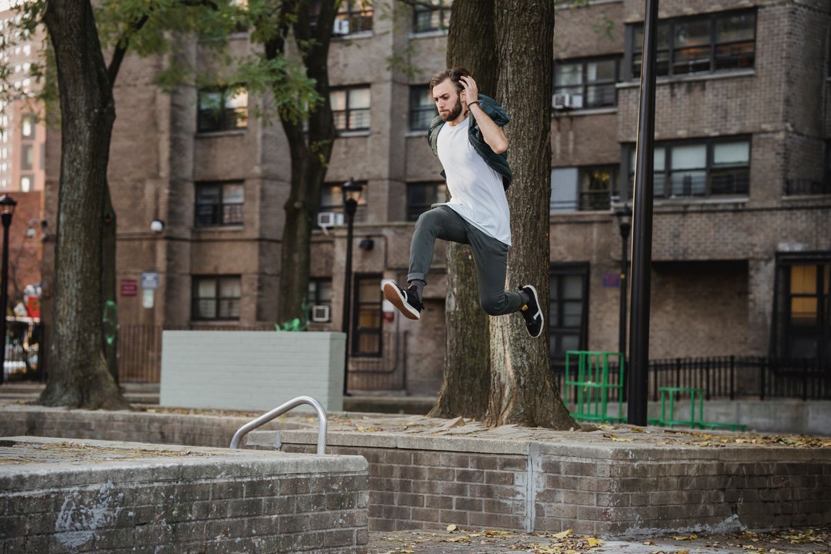 A traceur jumping between low brick walls in a tree-lined city park.