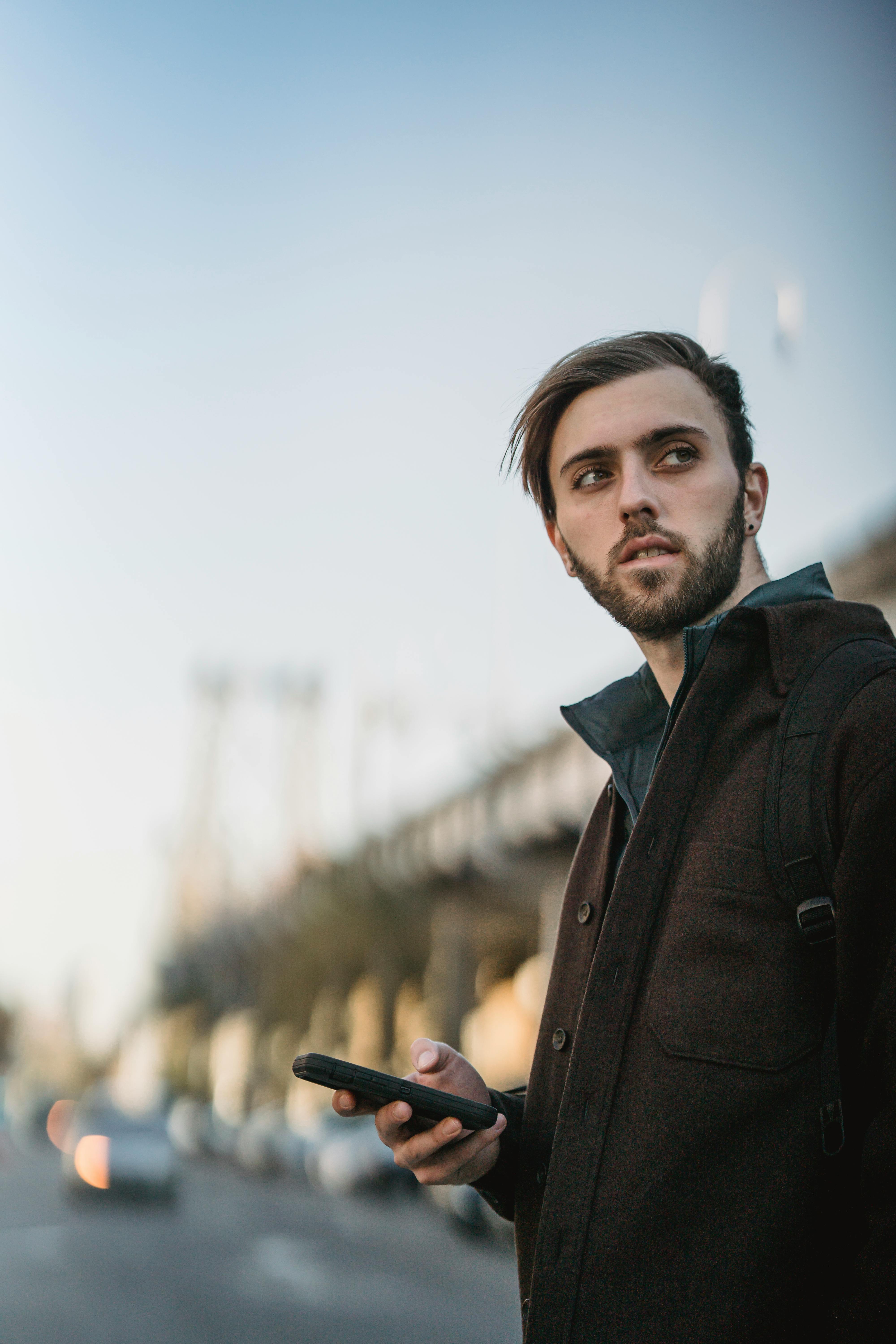 attentive bearded man with smartphone on urban roadway