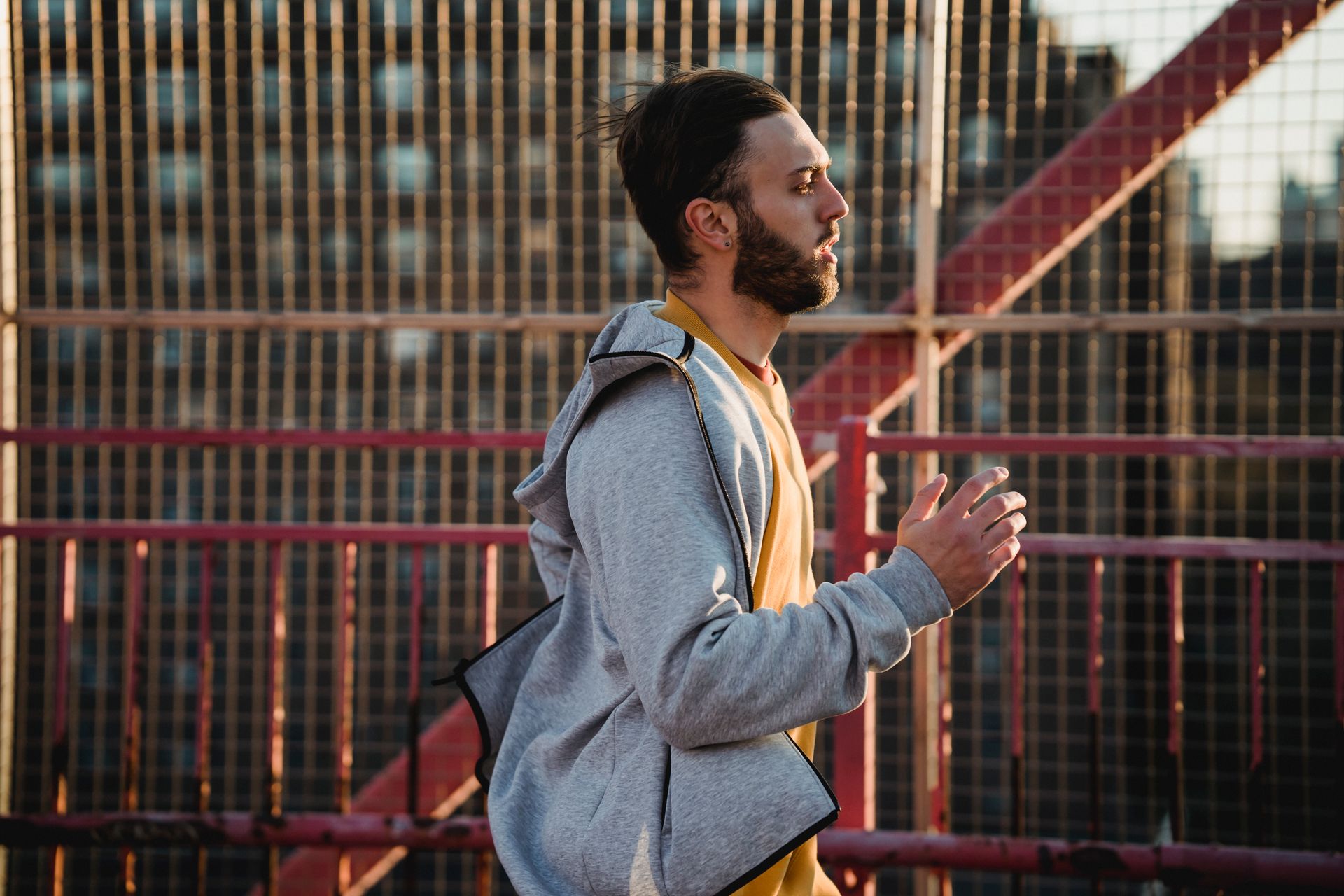 Side view of hipster sportsman in casual wear running near fence while looking forward in soft sunlight in town