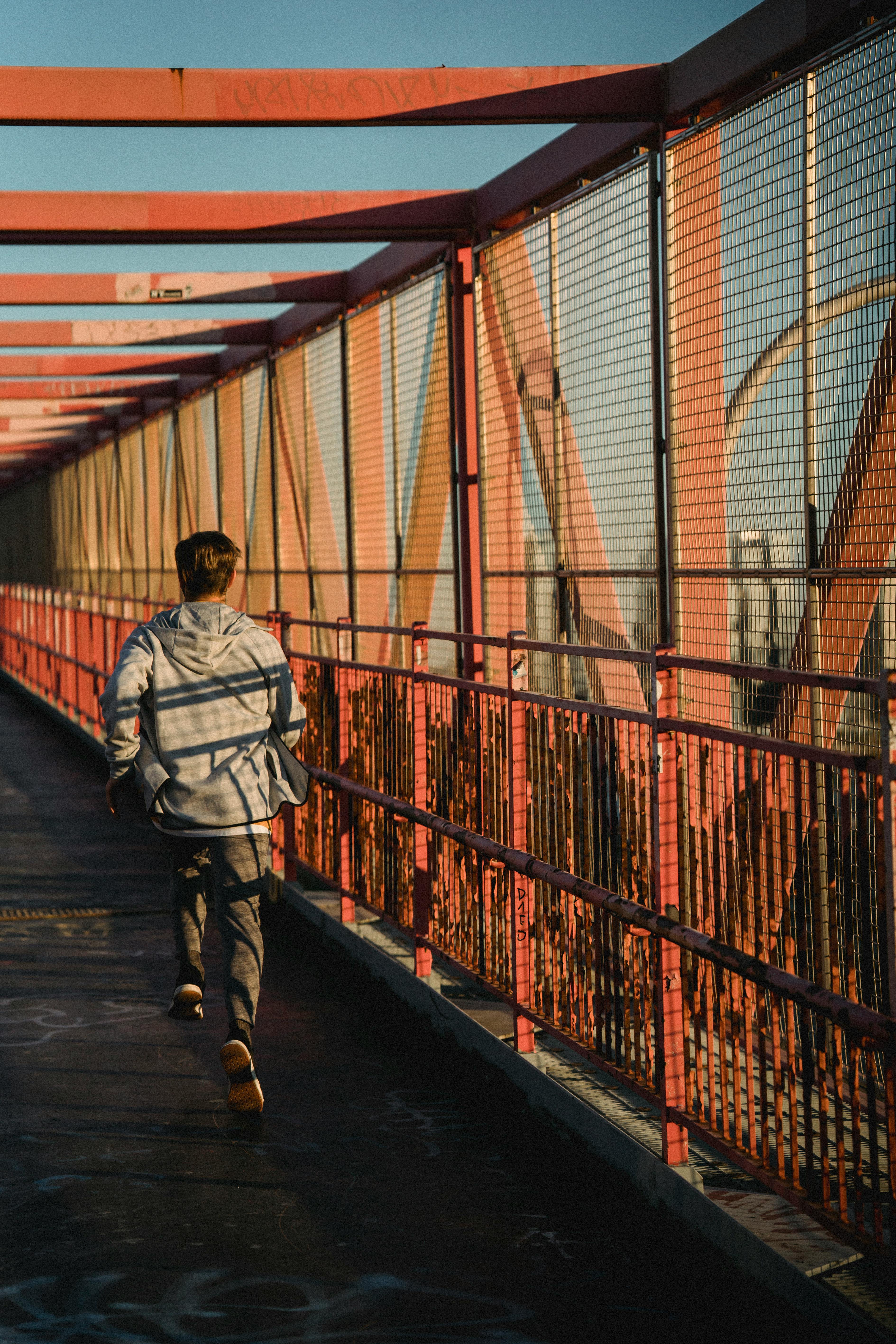 Back view of unrecognizable fit sportsman running on roofed bridge during training in city