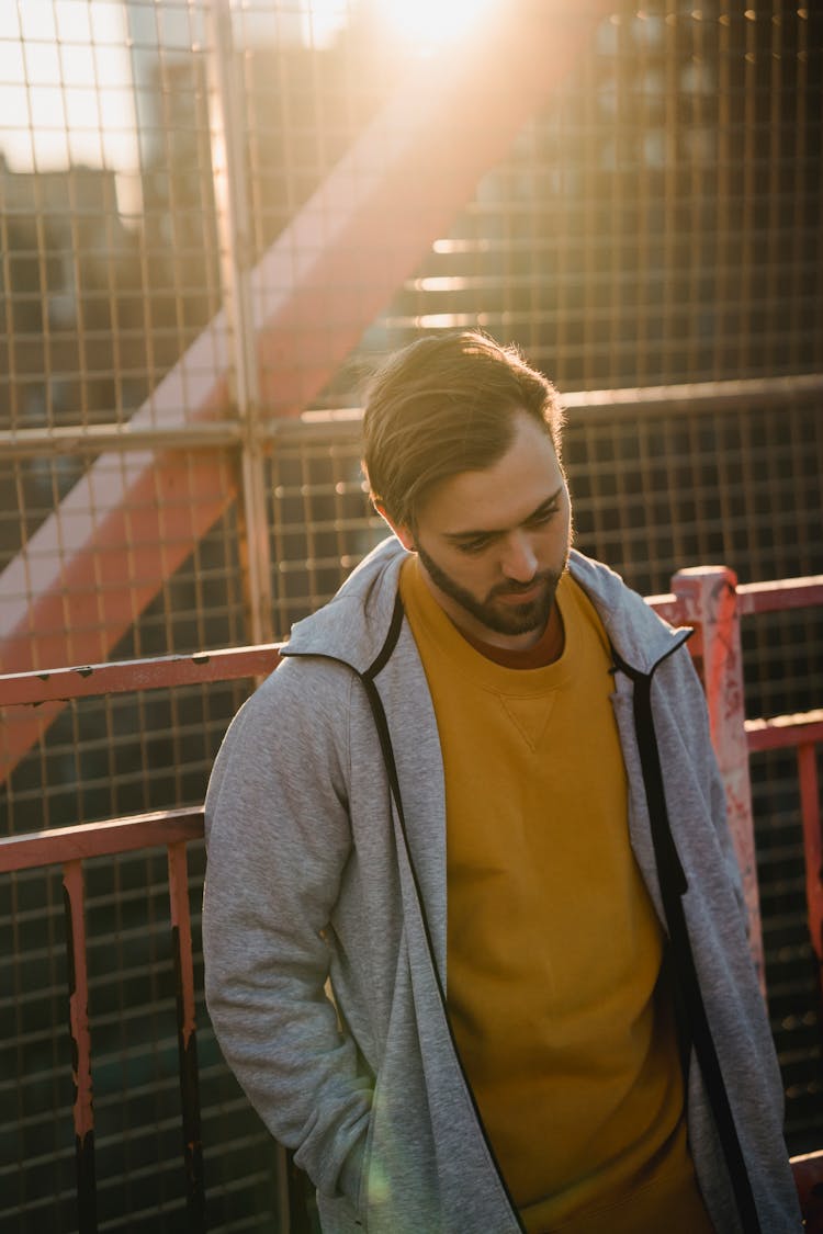 Melancholic Man Near Grid Fence In Sunlight