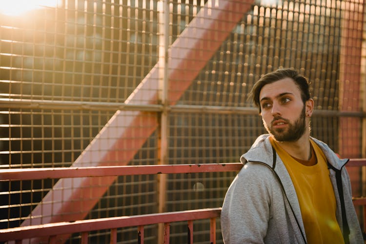 Dreamy Unshaven Man Near Grid Fence In Sunshine