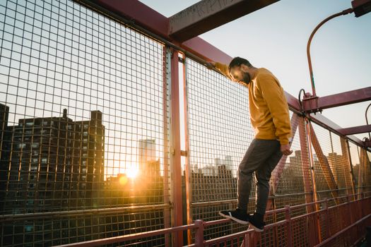Full body side view of active male standing on metal handrail near grid while training on bridge on sunny street