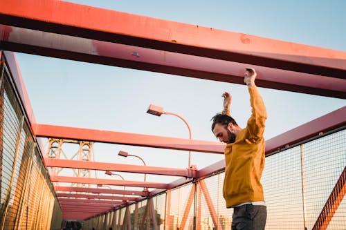 Free Side view of sportive male jumping off red metal structure on footbridge near metal fences while doing parkour exercises on street Stock Photo