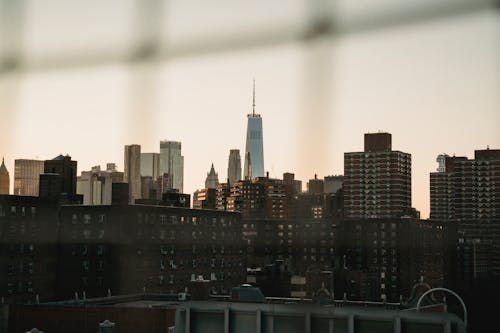 Through grid of cityscape with contemporary high skyscrapers and residential multistory buildings against cloudless sky in evening time in downtown