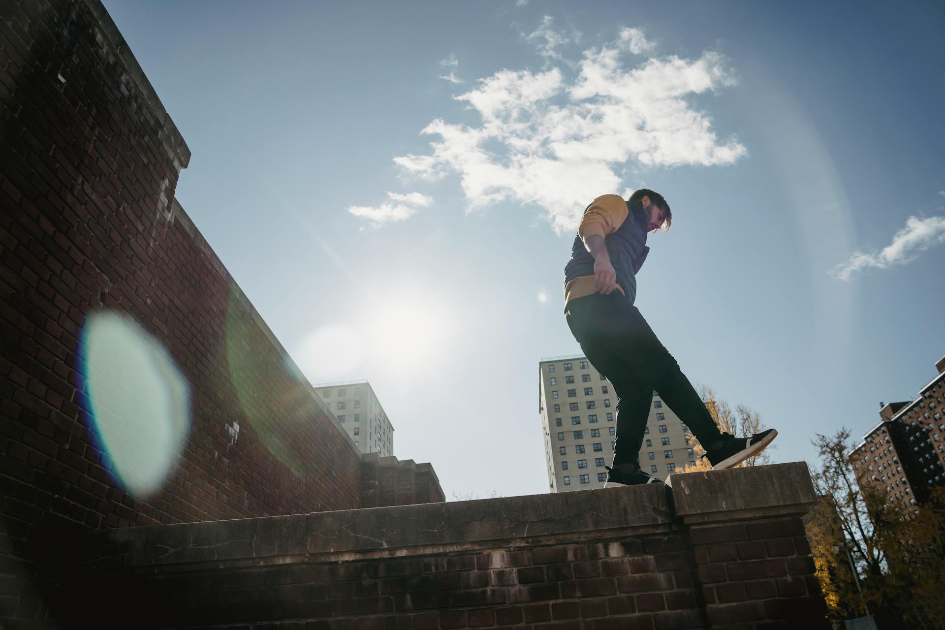 From below full body side view of energetic male standing on roof of brick construction against blue sky on street