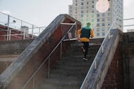 Back view full body of anonymous sportive male running on stairway while training on street against residential building