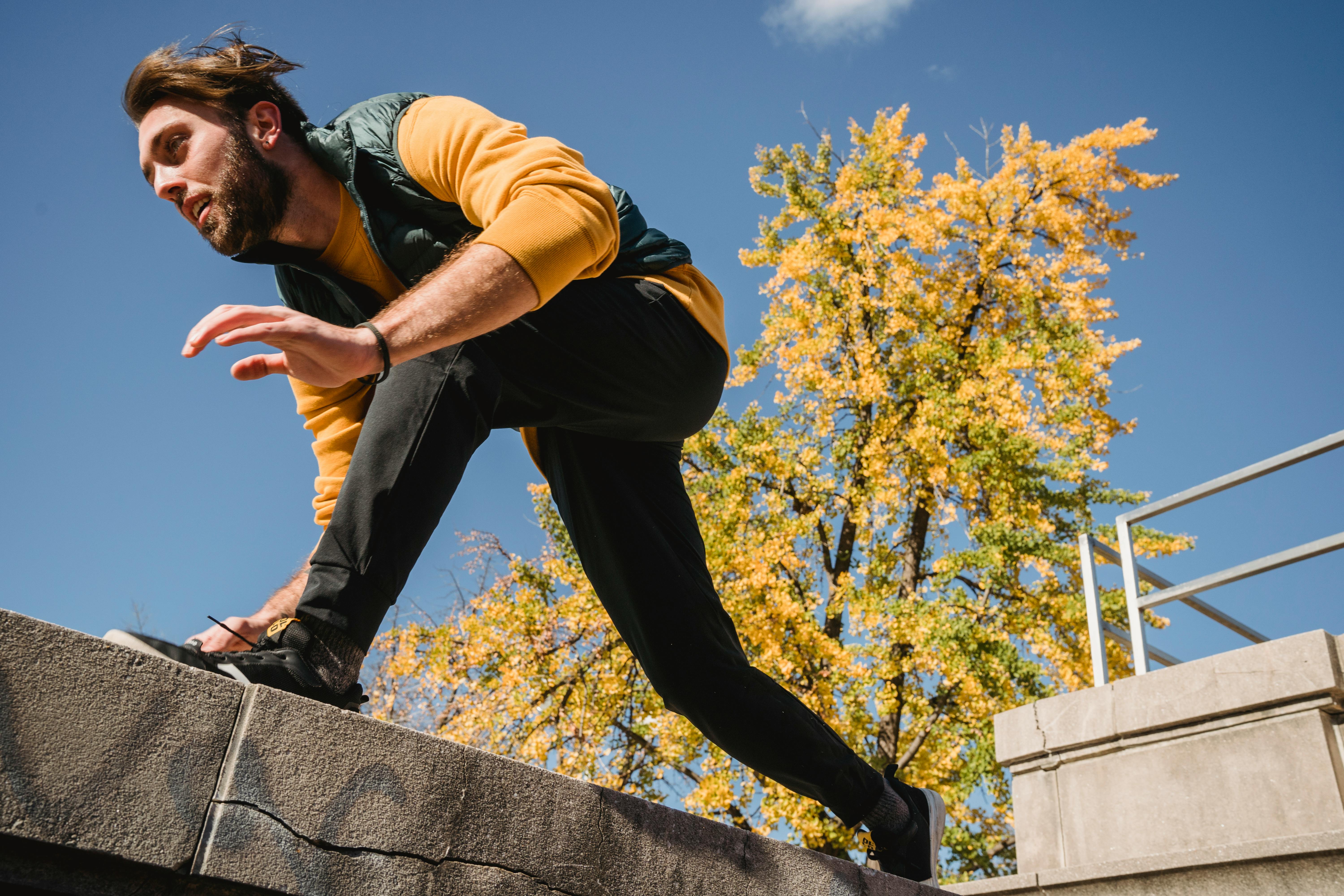 A man performing parkour on a ledge with autumn foliage in the background.