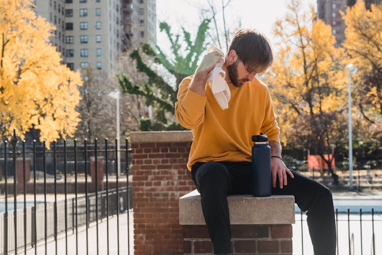 Tired Sportsman Sitting On Post With Bottle Of Water