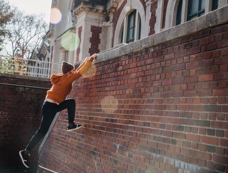 Side view full body of determined male in hat jumping on wall and grabbing onto railing during training on street