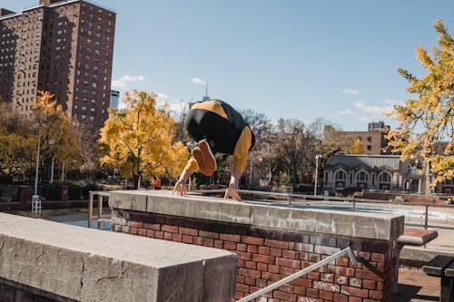Free Full body back view of anonymous sportive male jumping from wall during workout on sunny street with buildings and trees Stock Photo