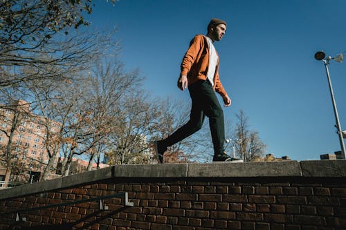 Hombre De Chaqueta Roja Y Blanca Y Pantalón Negro Sentado En El Muro De Hormigón