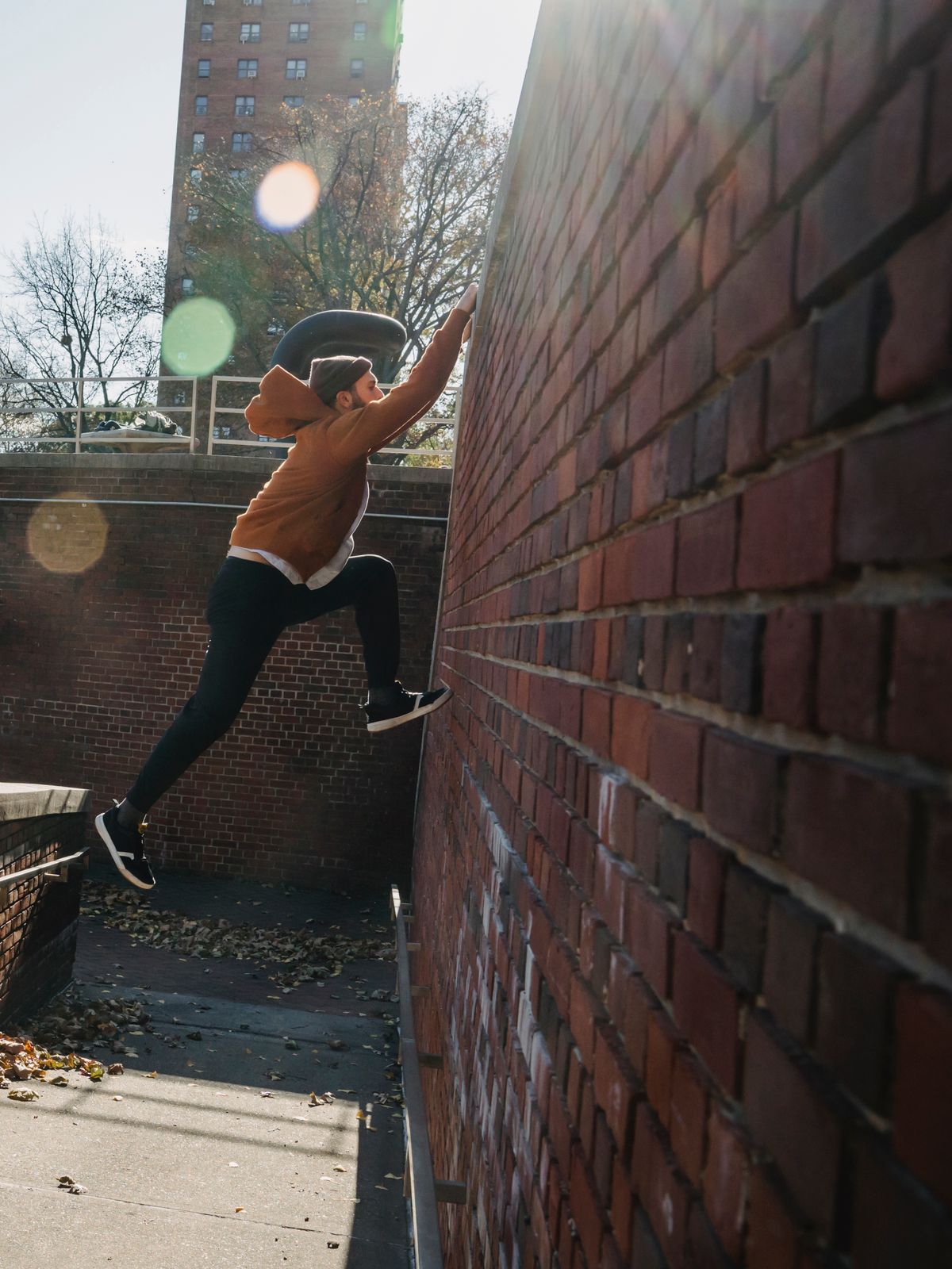 A traceur with one foot planted on a red brick wall, reaching up for the top edge.