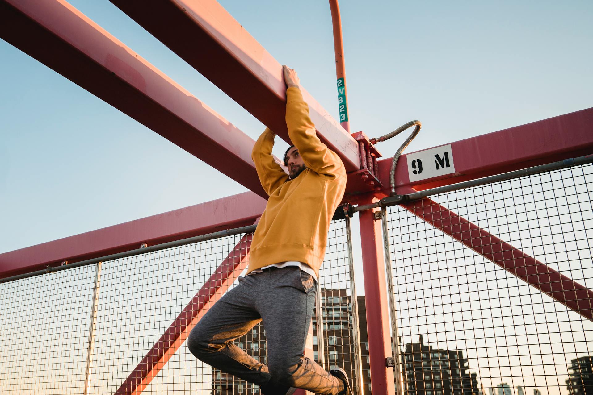 Hipster man hanging on beam of urban bridge during training