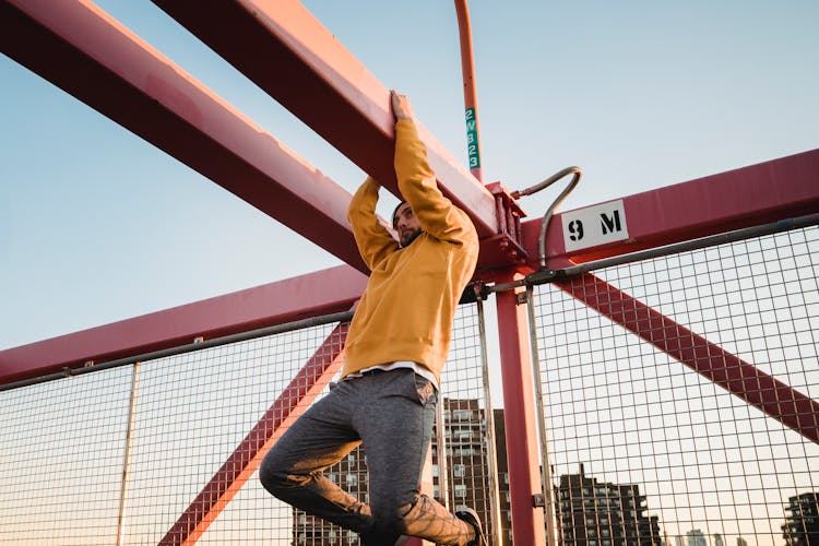 Hipster Man Hanging On Beam Of Urban Bridge During Training