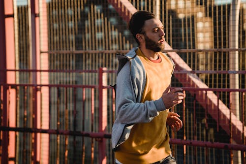 Homme En Veste Zippée Bleue Et Short Jaune Debout Près D'une Clôture En Métal Rouge