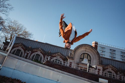 From below of sportsman jumping in air while demonstrating upside down trick during training against urban building