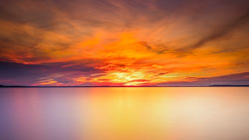 Free A stunning sunset over a calm sea, with vibrant orange and yellow hues reflecting in the water. Stock Photo