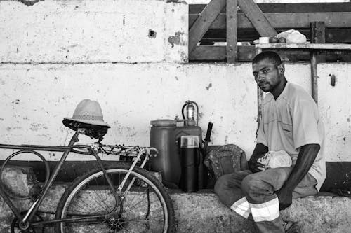 Grayscale Photo of a Man Sitting Near the Bicycle 