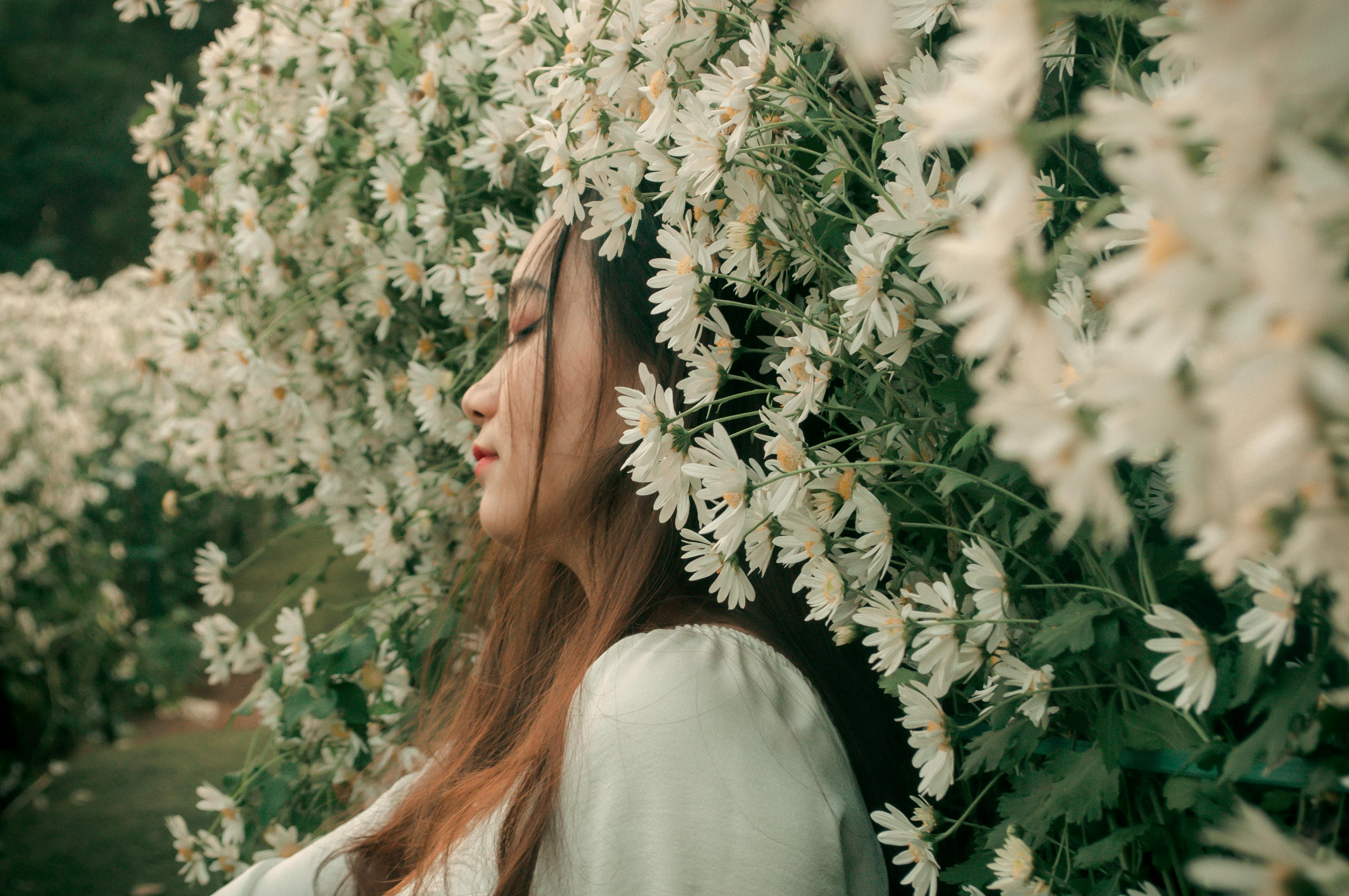 Peaceful portrait of a woman surrounded by blooming daisies, eyes closed in serenity.