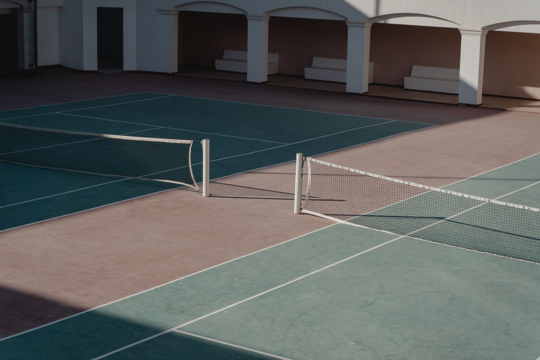 A deserted tennis court with shadows casting over the net, creating a serene atmosphere.