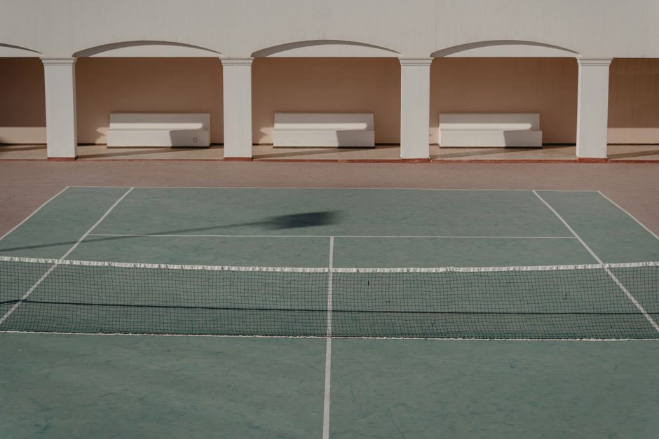 Minimalist view of an empty tennis court with benches, captured outdoors in daylight.