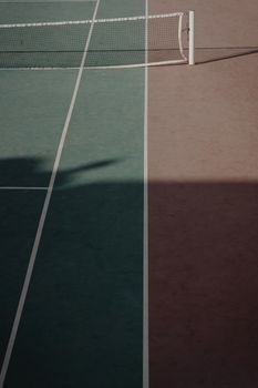 A minimalist view of a tennis court showing a net and contrasting sun and shadow divisions.