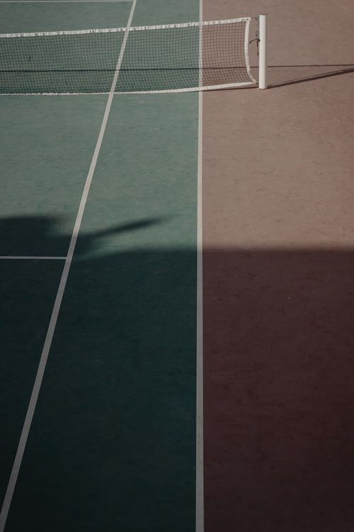 Free A minimalist view of a tennis court showing a net and contrasting sun and shadow divisions. Stock Photo