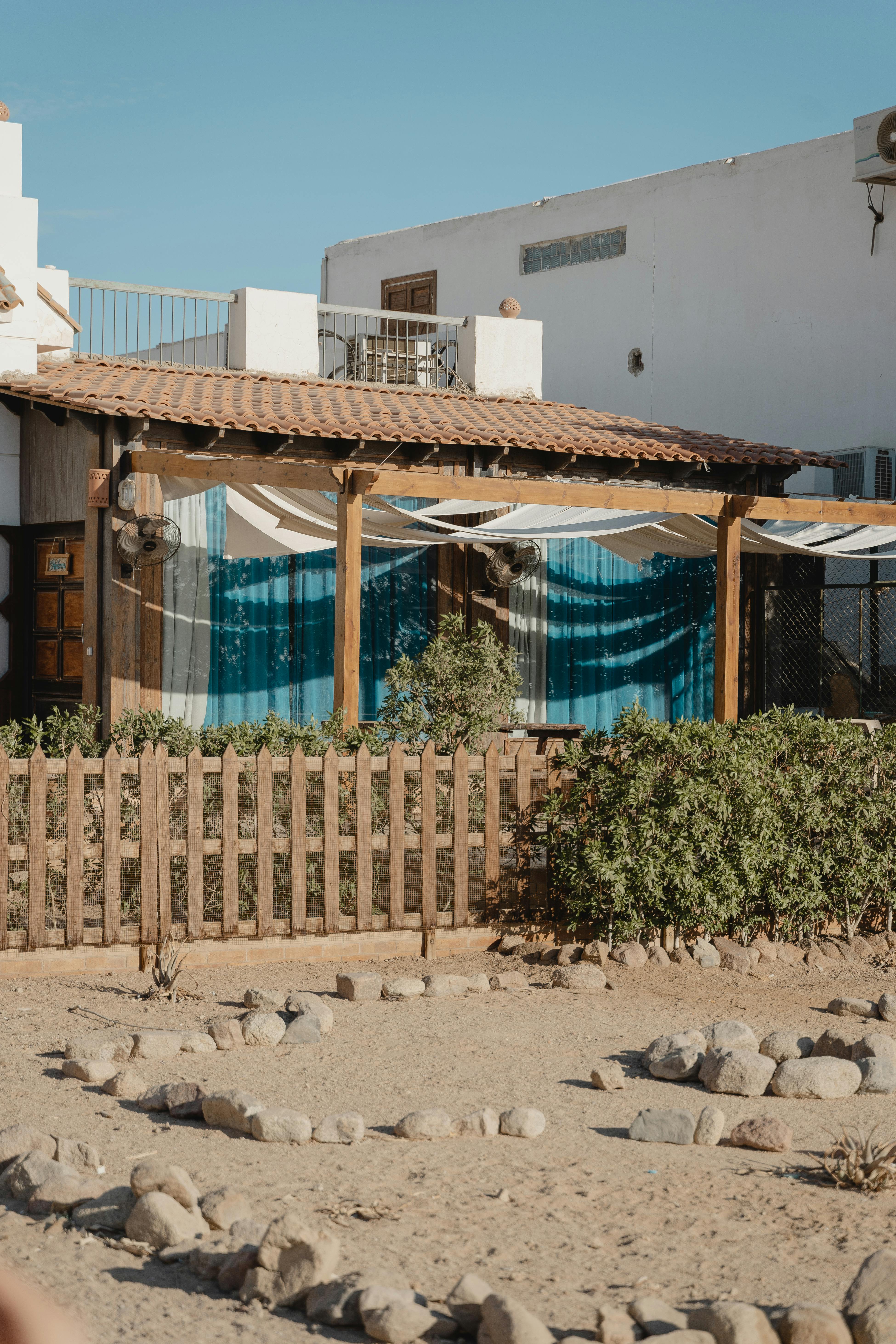 Charming Mediterranean house with wooden fence and plants under clear blue sky.