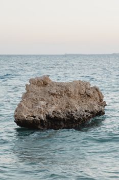 A large rock formation in a serene ocean setting under a soft sky.