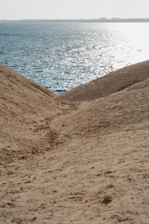 Free Golden sand dunes meet the shimmering ocean under a bright sky, creating a tranquil coastal scene. Stock Photo