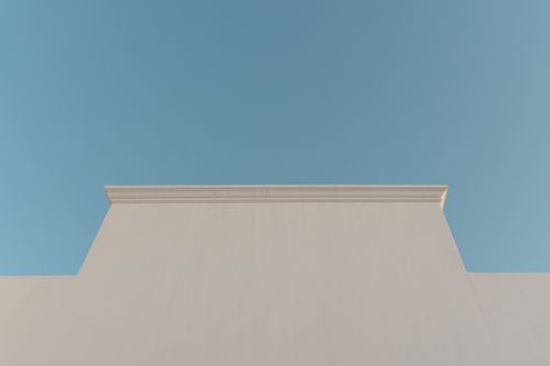 Free Simple minimalist facade of a white building set against a clear blue sky, emphasizing symmetry. Stock Photo