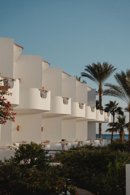Free Elegant resort featuring white facades and palm trees under a blue sky, perfect for tropical vacations. Stock Photo
