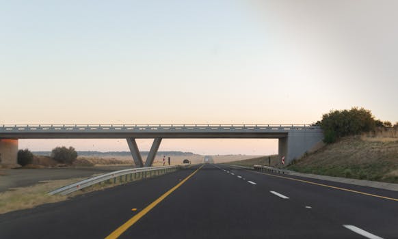 A peaceful highway stretches under a bridge at sunset, offering a tranquil travel experience.