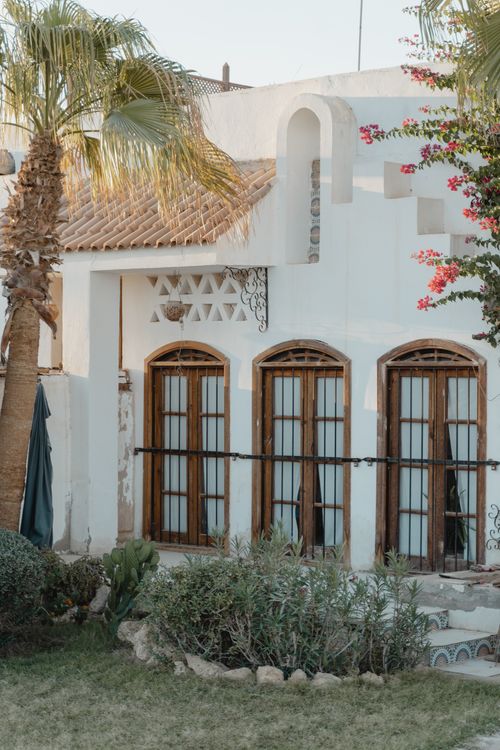Free A picturesque Mediterranean-style building with wooden arched windows and lush greenery showcasing architectural elegance. Stock Photo