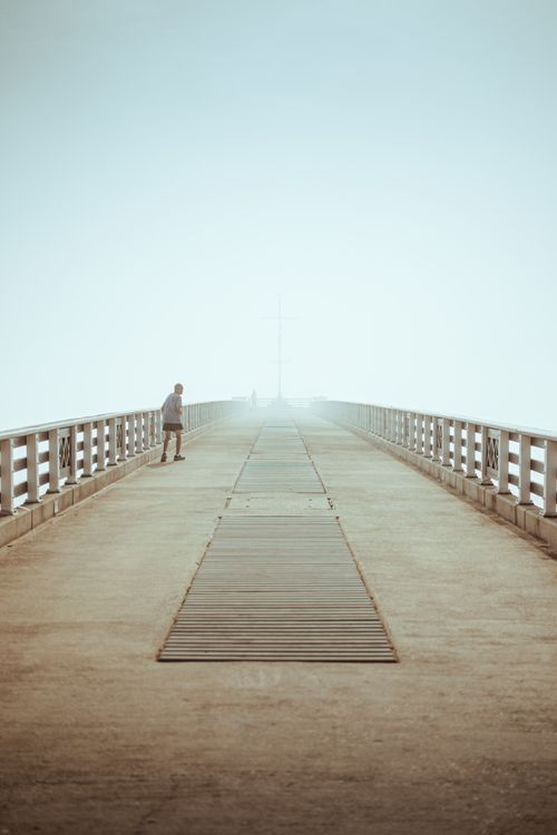 Free A solitary person strolls along a foggy pier during sunrise, creating a peaceful and symmetrical scene. Stock Photo