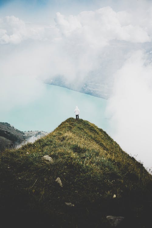 A Person Standing on a Grassy Cliff near the Clouds