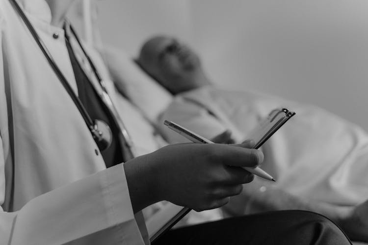 Doctor Holding A Medical Chart Sitting Beside A Patient