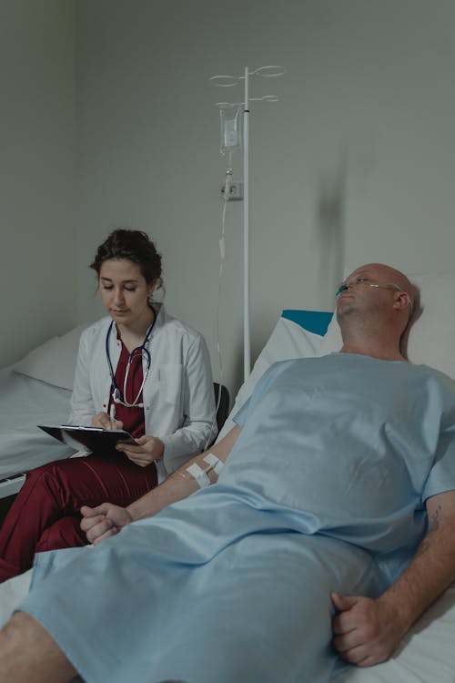 Doctor Writing on Medical Chart while Sitting beside a Patient