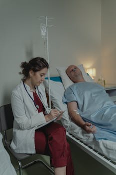 A doctor sits beside a patient in a hospital room, taking notes.