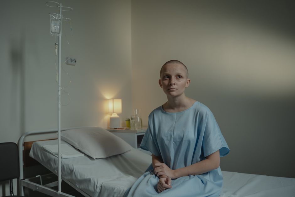 A thoughtful woman in a hospital gown sits on a bed, conveying calmness and reflection.