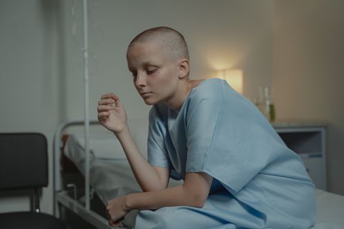 Free Bald woman sitting in a hospital gown, depicting sadness and contemplation. Stock Photo